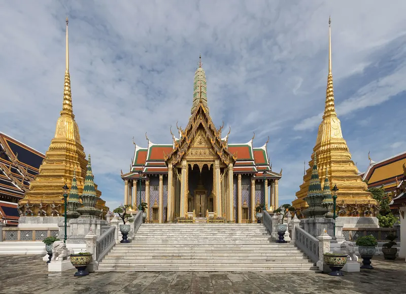 Escalinata blanca hacia el Panteón Real, de techos rojos y aguja dorada, entre dos chedis dorados, en Wat Phra Kaew (Gran Palacio).