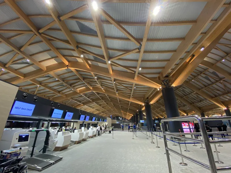 Sala de salidas del aeropuerto de Clark, con techo ondulado de vigas de madera, columnas oscuras y mesones para despachar equipaje.