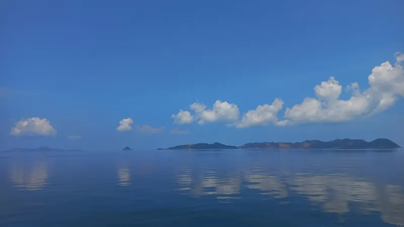 Mar en calma muy azul con una hilera de islas bajas en el horizonte y nubes blancas reflejadas en el agua.