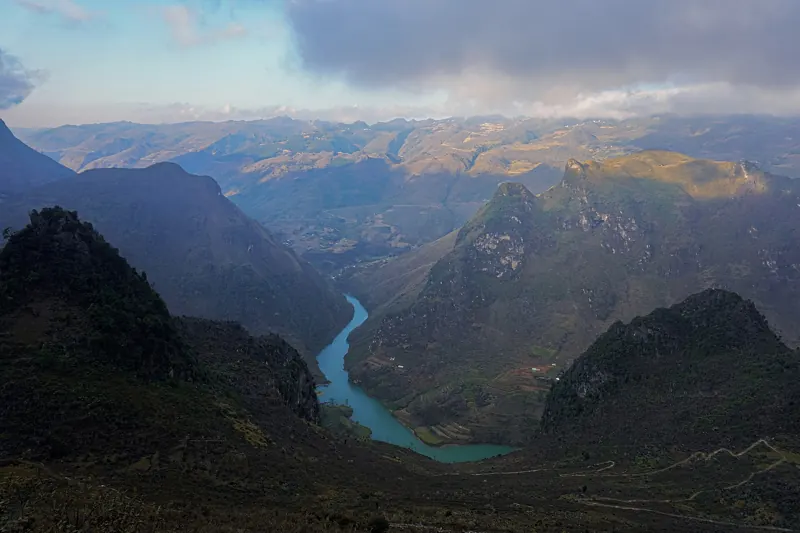 El río Nho Que, de color jade, serpentea por el fondo de un cañón profundo entre montañas de roca, bajo un cielo nublado.
