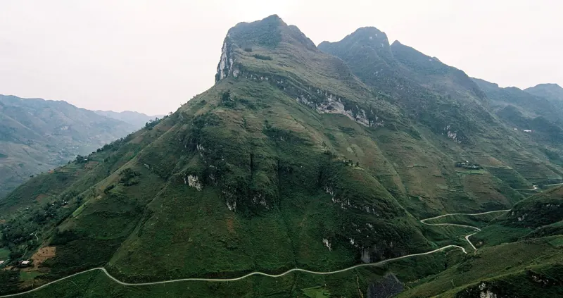 Una carretera angosta serpentea por la ladera de una montaña verde y rocosa en el paso de Ma Pi Leng.