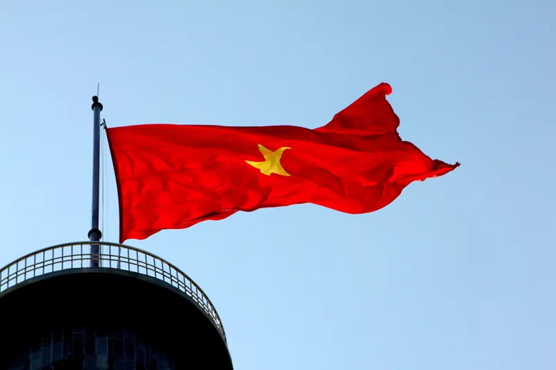 Gran bandera roja de Vietnam con estrella amarilla ondeando sobre la cima de la torre de Lung Cu, contra un cielo azul.