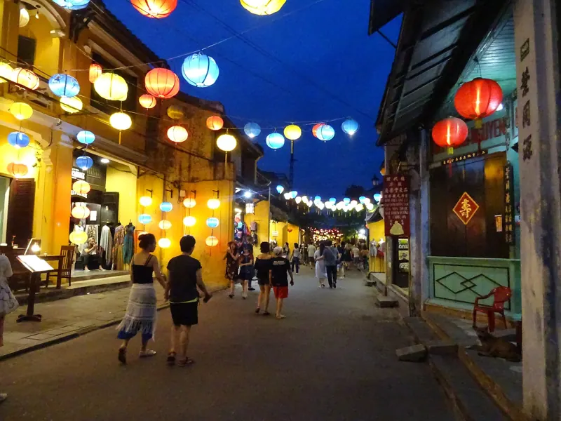 Calle de Hoi An al anochecer, con faroles de colores colgados sobre la calle, casas amarillas y gente paseando.