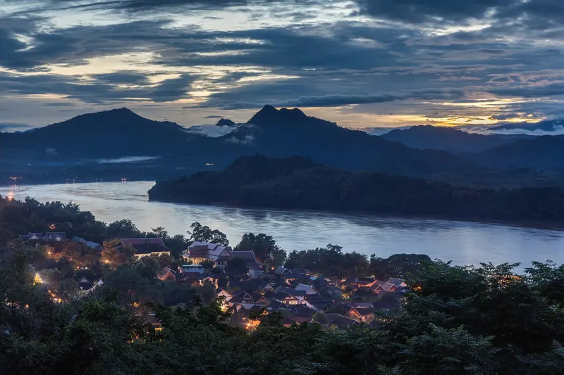 Al anochecer, el Mekong pasa entre cerros oscuros y las primeras luces de Luang Prabang, vistos desde el monte Phousi.