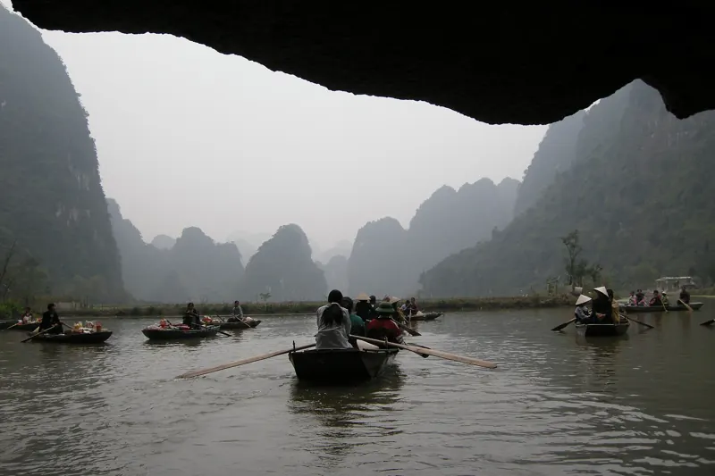 Vista desde la boca de una cueva: botes a remo con pasajeros en un río rodeado de cerros de roca caliza entre la neblina.