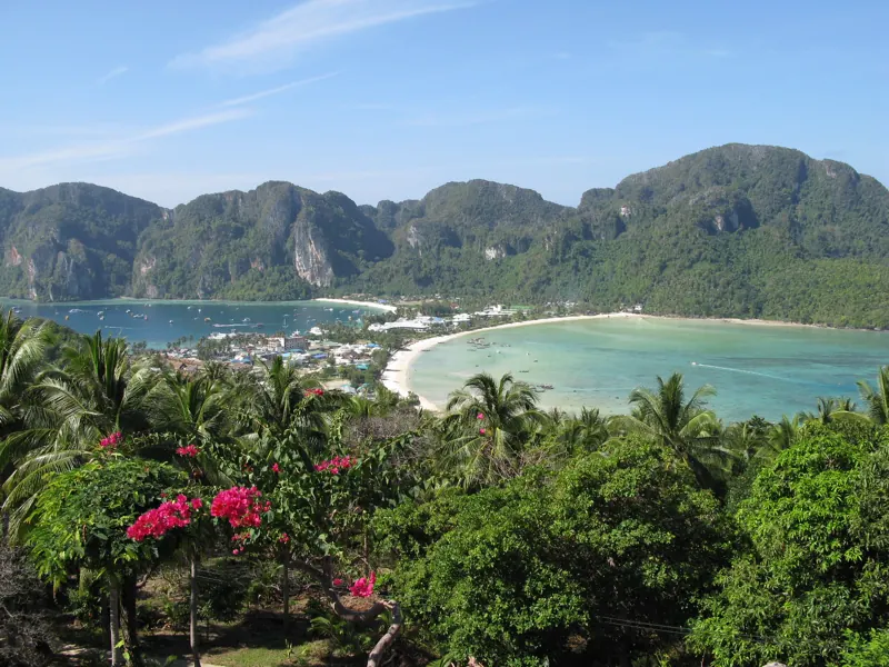 Desde el mirador de Phi Phi Don: dos bahías turquesa separadas por una franja de tierra con el pueblo, cerros verdes y flores fucsia.