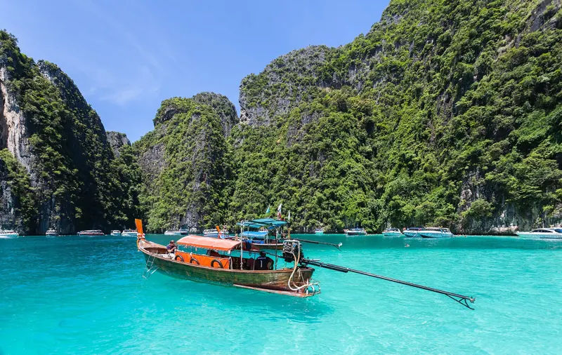 Un longtail de madera flota en agua turquesa entre acantilados cubiertos de selva en la isla Phi Phi Leh.