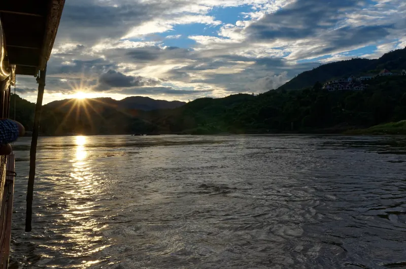El sol se pone tras cerros de selva y brilla sobre el Mekong, visto desde un costado del bote cerca de Pakbeng.